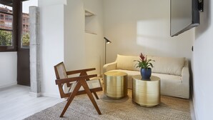 A modern living room with a sofa, two round side tables, a floor lamp, and a large window with a view of buildings. - Canvas Apartments & Lofts Girona, Situados en el río Onyar (Girona)