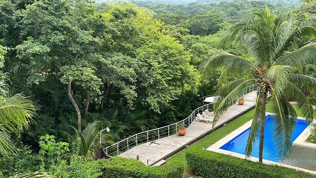 A pool surrounded by lush greenery, a concrete deck, and a white railing. - Condo Marimba, near Sámara and Carrillo beach (Sámara)