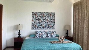 A hotel room with a bed, two nightstands, a ceiling fan, a wall with a floral artwork, and a window with curtains. - Condo Marimba, near Sámara and Carrillo beach (Sámara)