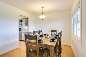 A dining area with a wooden table set for six, surrounded by chairs. A chandelier hangs from the ceiling, and a window provides natural light. - Relax Fireside! Home < 1 Mi to Tryon International (Mill Spring)