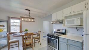 Een moderne keuken met witte kastjes, een roestvrijstalen fornuis en een magnetron. Er staat een eettafel met stoelen en daarboven een kroonluchter.