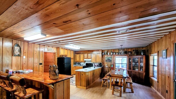 A spacious kitchen with wooden cabinets, a central island, and a dining area with rustic wooden furniture. - COZY CABIN/GREAT RATES!! Acreage to walk. Pond views. MAX 8 guests, No Pets (Broken Bow)