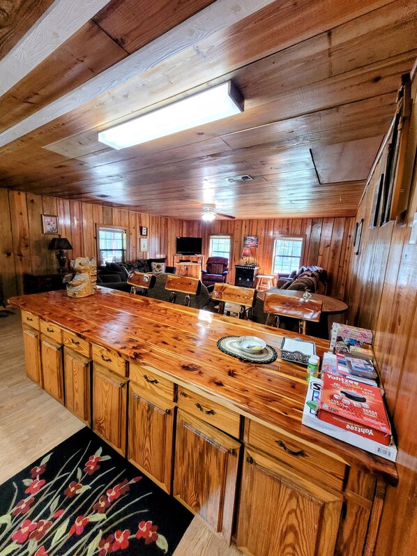 Un interior de madera con una zona de bar central, varias opciones de asientos y un televisor.