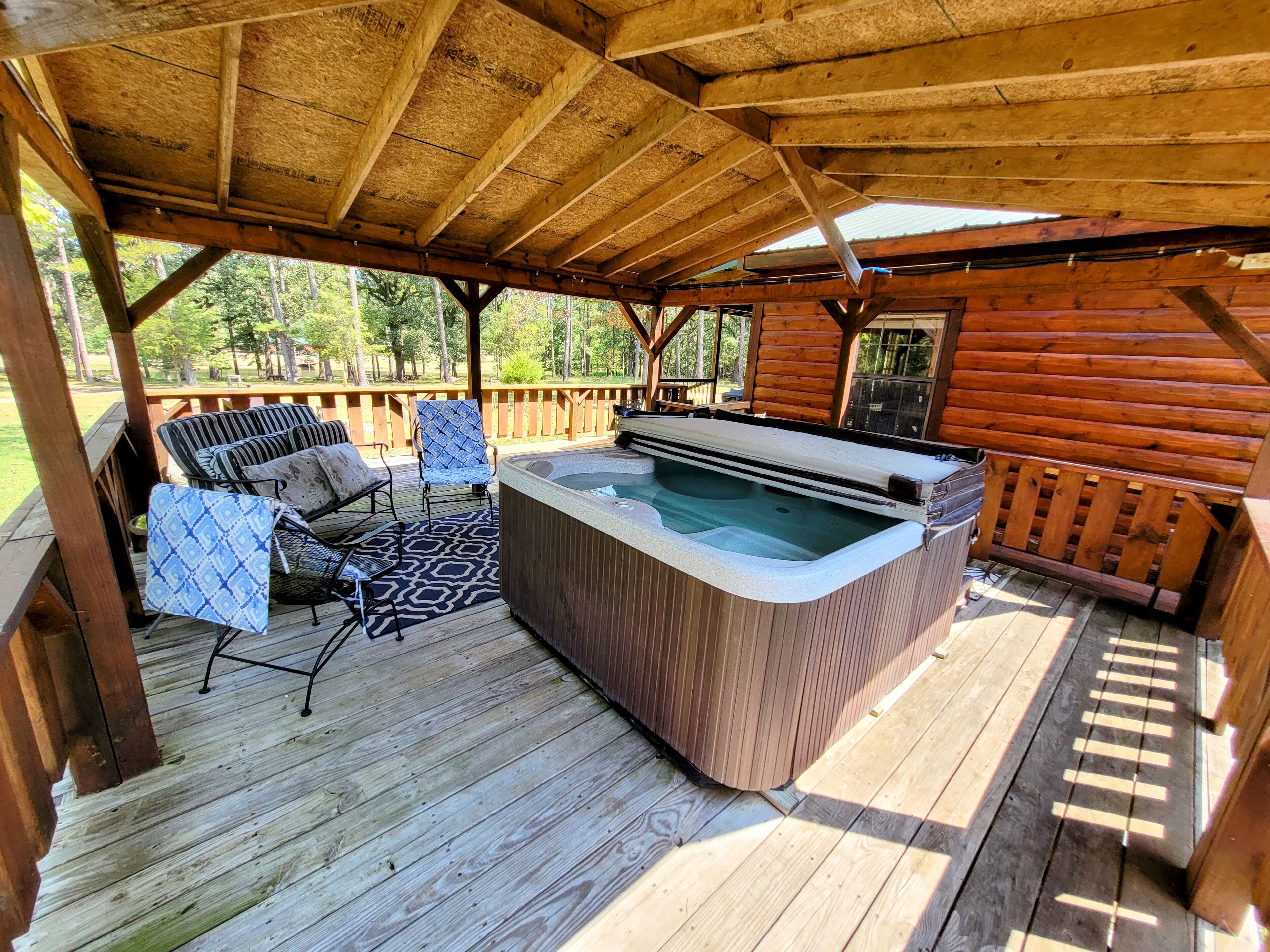 A wooden deck with a hot tub, outdoor furniture, and a view of the surrounding forest.
