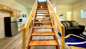 Un escalier en bois menant à un niveau supérieur dans un espace intérieur moderne comprenant une cuisine et un salon.
