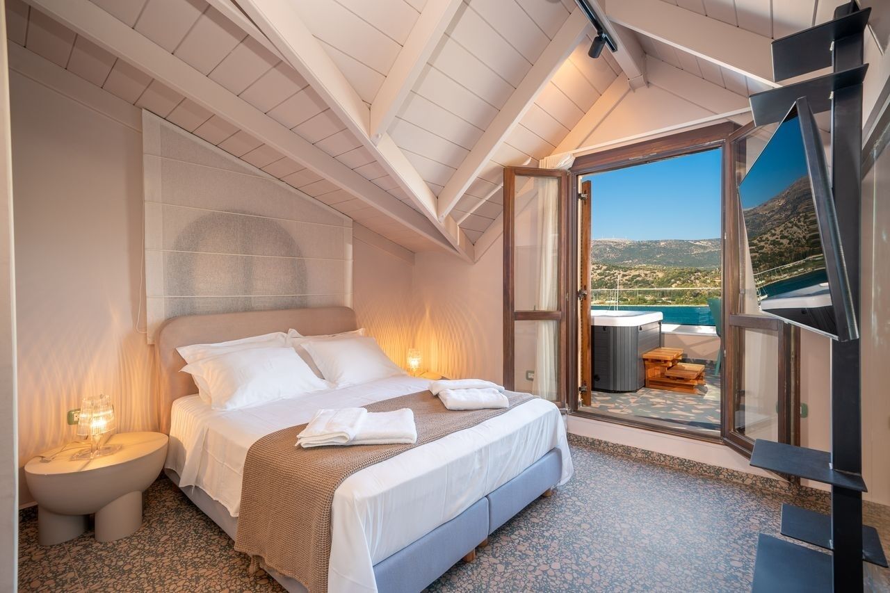 A bedroom with a bed, bedside table, and a view of a mountainous landscape through a glass door.