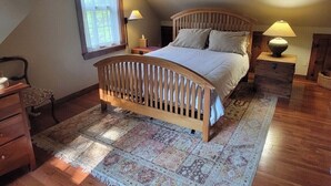 A bedroom with a sloped ceiling, a wooden bed frame, a patterned rug, and two bedside lamps.