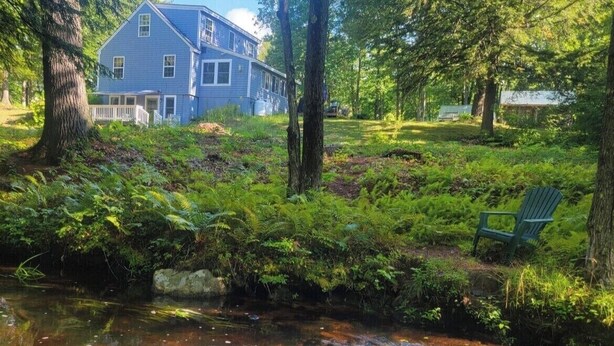 A house surrounded by a lush green landscape with a small stream in the foreground.