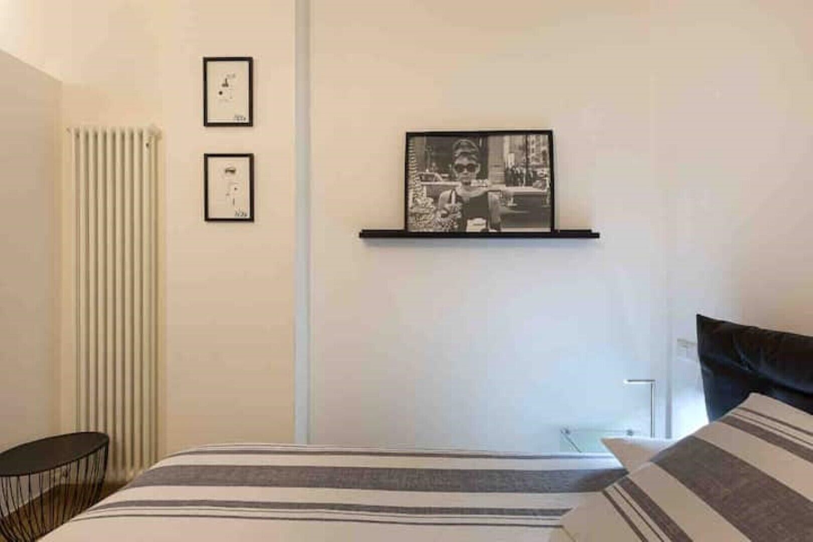 A bedroom with a bed, a radiator, and two framed pictures on the wall.