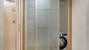 Ein Badezimmer mit Duschkabine aus Glas, Toilette und Waschmaschine.