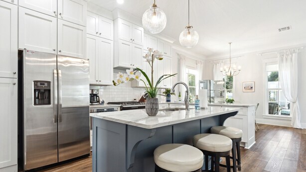 A modern kitchen with white cabinets, a stainless steel refrigerator, a marble island with stools, and pendant lighting. - Classic Coastal Cottage ~ Steps to the Beach! 4-Seater Golf cart for rent! (Bay St. Louis)