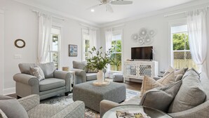 A living room with grey sofas, a coffee table, and a TV on a white cabinet. - Classic Coastal Cottage ~ Steps to the Beach! 4-Seater Golf cart for rent! (Bay St. Louis)