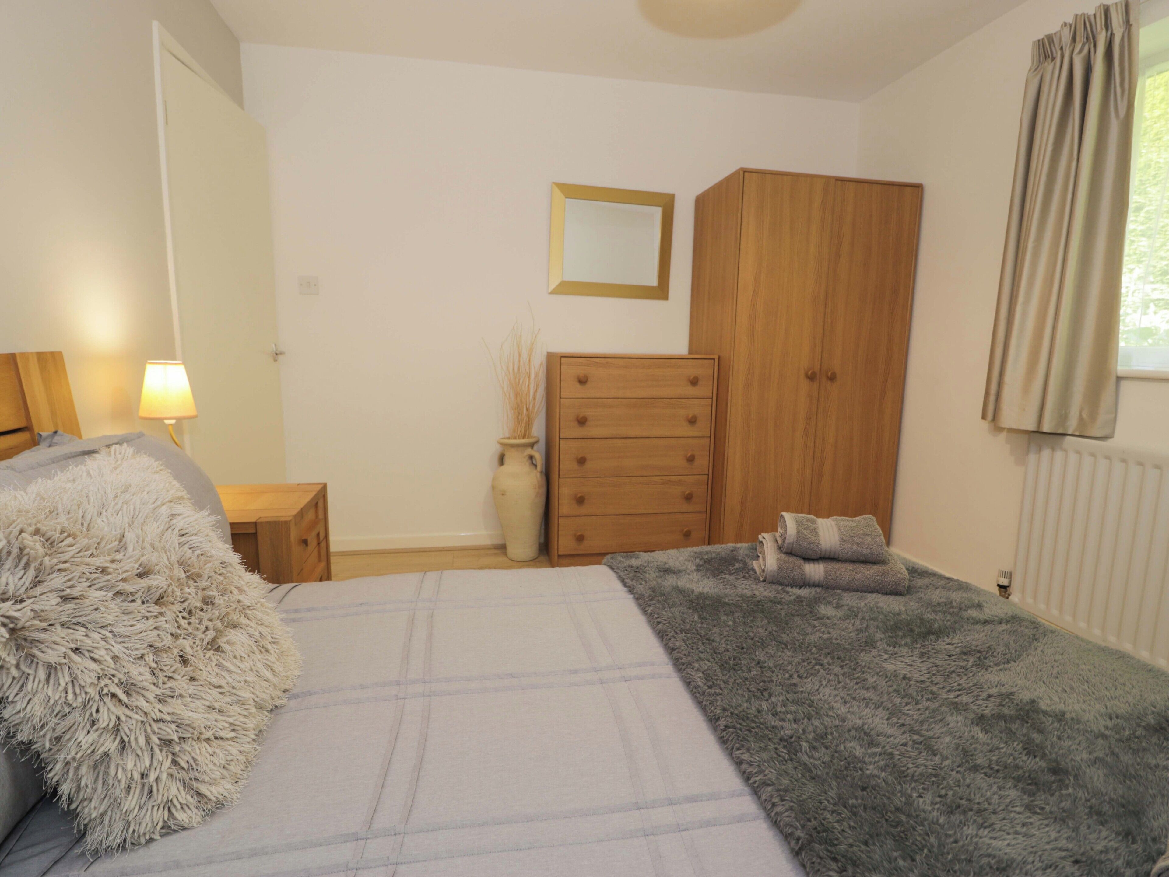 A bedroom with a bed, a dresser, a mirror, a lamp, and a radiator.