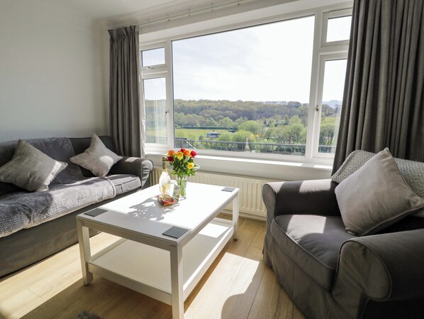 A living room with two grey sofas, a white coffee table, and a view of a green landscape through large windows. - Trem Y Foel (Penrhyndeudraeth)