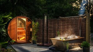 Una sauna de madera con un banco en el interior, un jacuzzi y una valla de bambú en un jardín.
