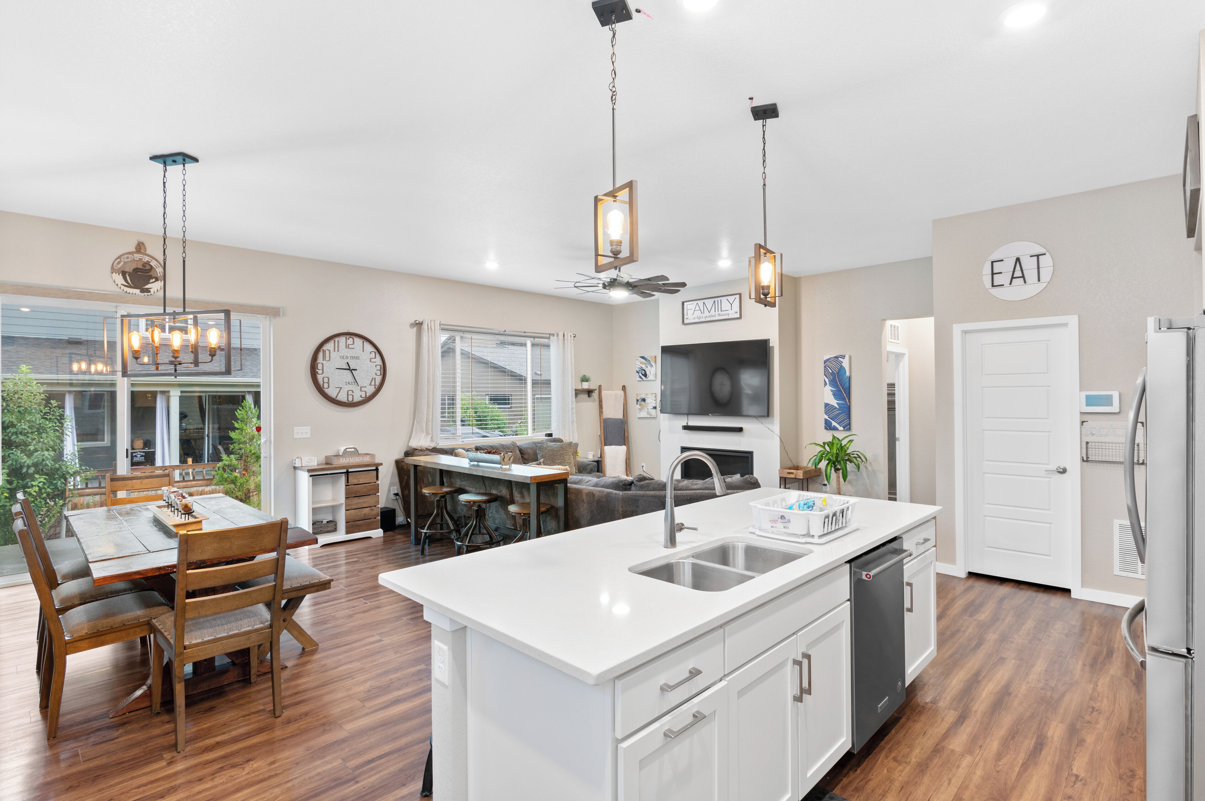 A modern kitchen with white cabinetry, a central island with a sink, and a dining area with wooden chairs and a table.