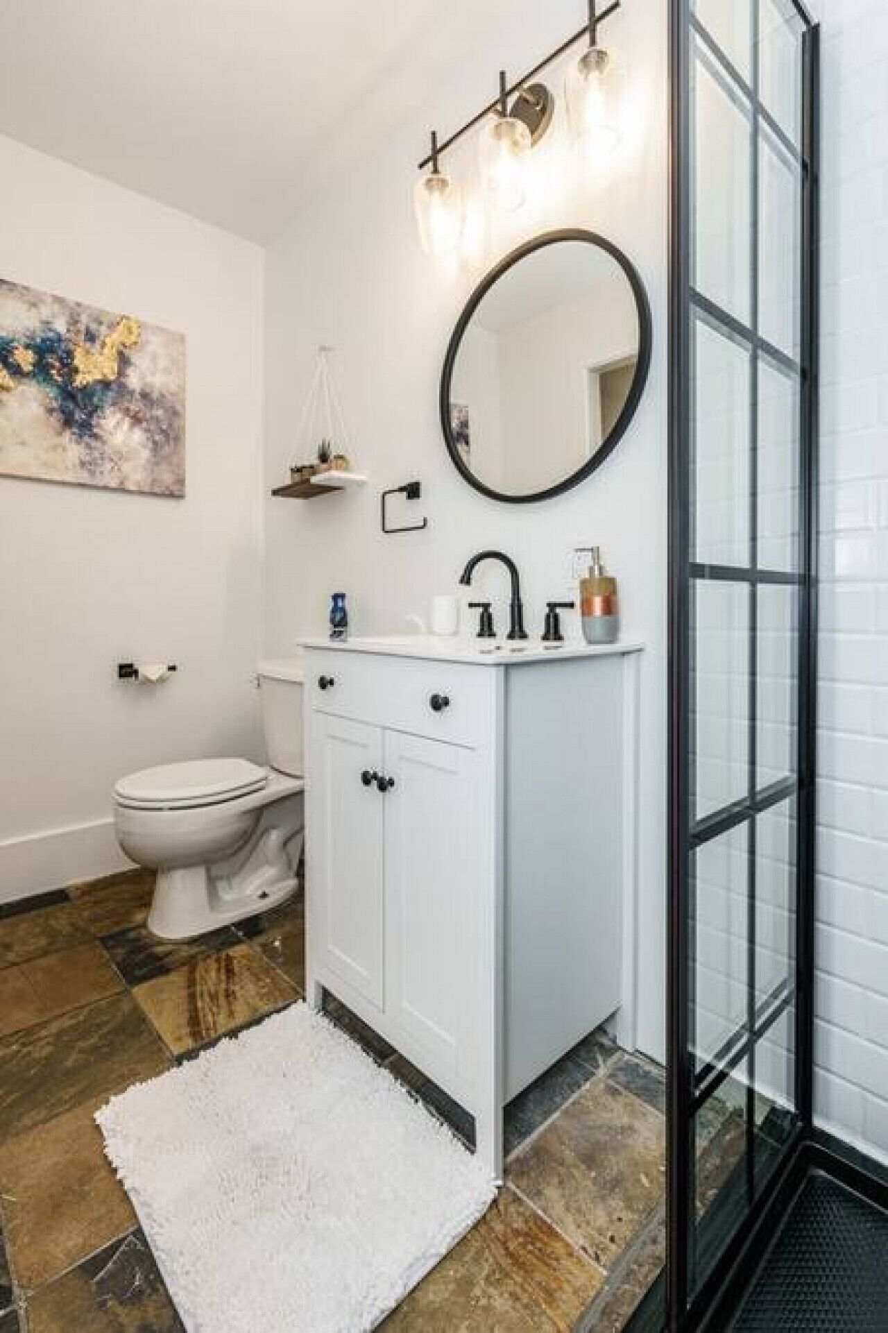 Een badkamer met een wit wastafelmeubel, een ronde spiegel, een douchecabine met glazen wanden en een betegelde vloer.