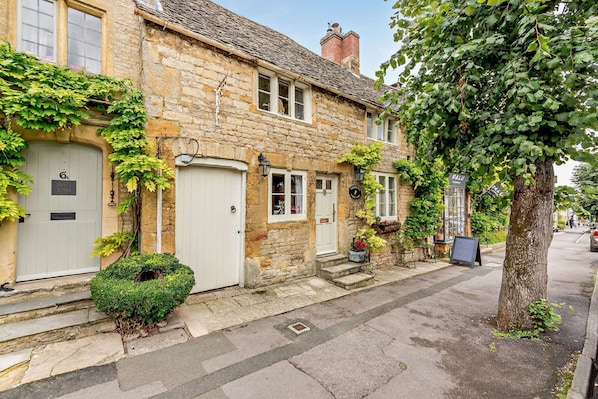 A stone building with a white door, a small garden, and a tree.