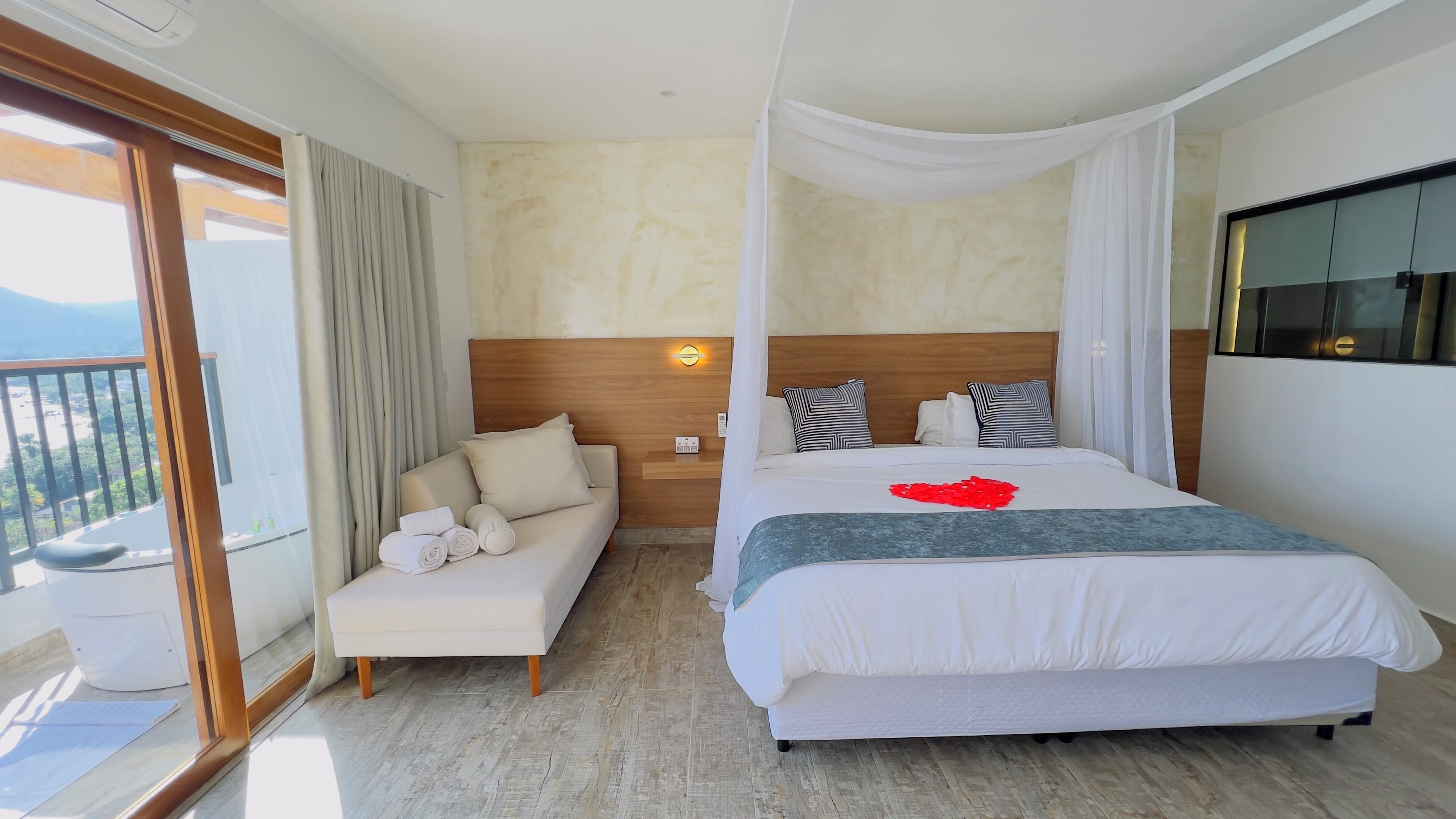 A hotel room with a large bed, a sofa, a balcony with curtains, and a view of the mountains.