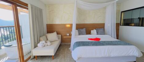 A hotel room with a large bed, a sofa, a balcony with curtains, and a view of the mountains.