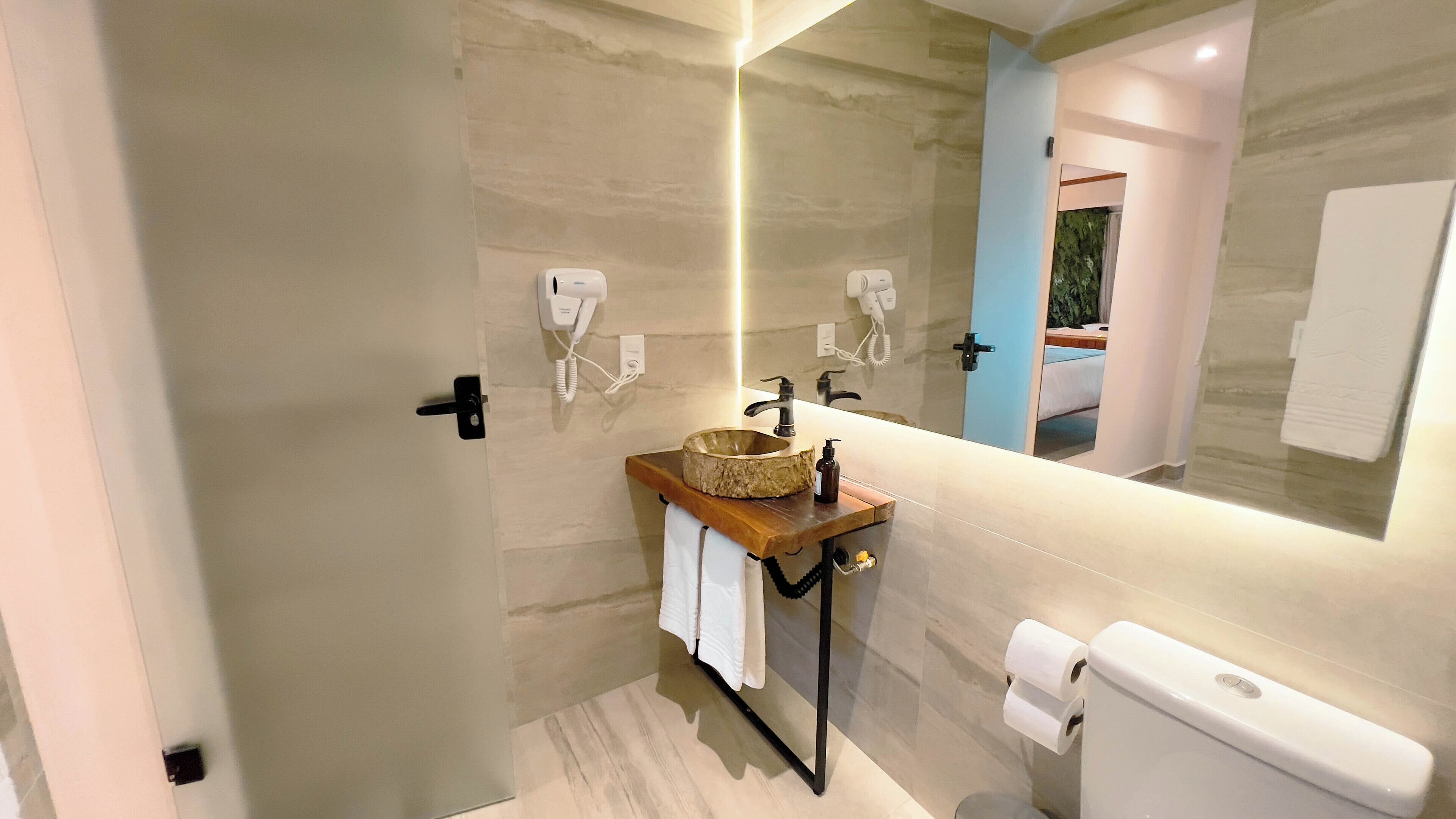 A modern bathroom with a stone sink, a large mirror, a toilet, and a shower area.