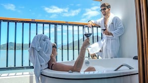 A person relaxing in a bathtub on a balcony with a view of a lake and mountains. - Catalina Hotel (Ubatuba)