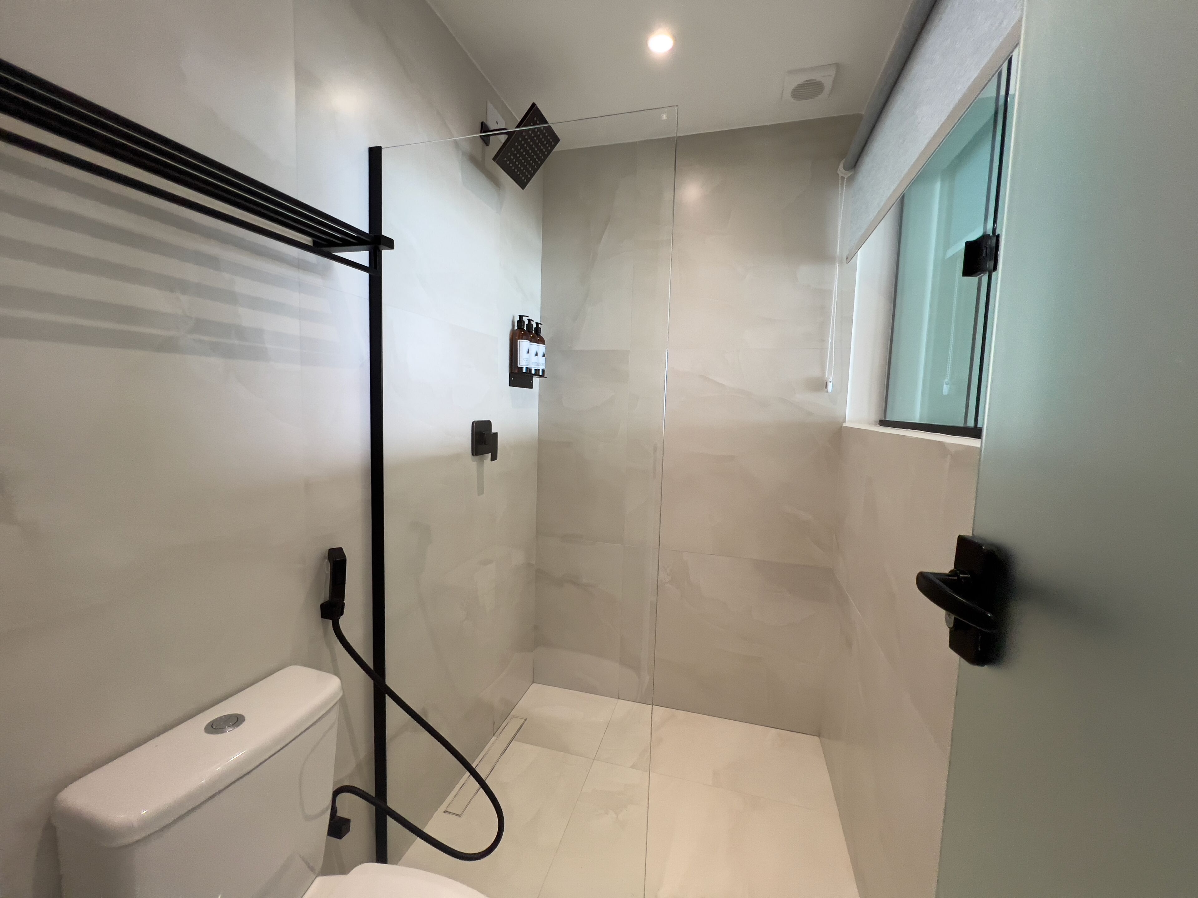 A modern bathroom with a glass shower enclosure, a toilet, and a window.