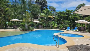 A pool area with lounge chairs and umbrellas, surrounded by lush greenery. - Beautiful 2bd 2 ba villa w/lush yard, gated community 15 min from Manuel Antonio (Quepos)