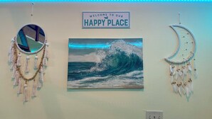 Eine Wand mit einem Schild, das 'Welcome to Our Happy Place' zeigt, einem Traumfänger und einem Wellenbild.