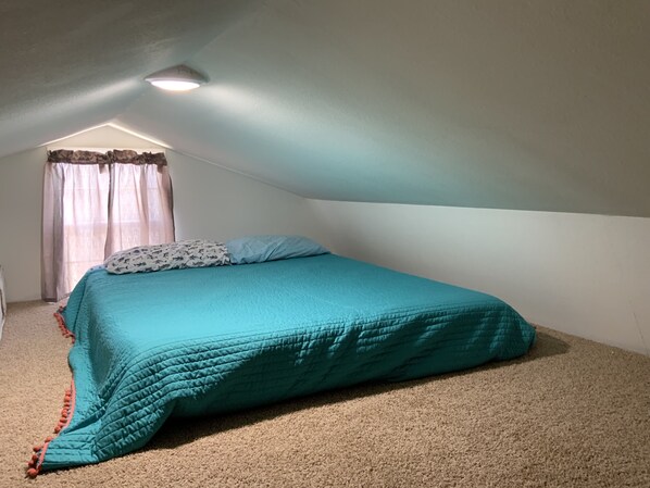 Een slaapkamer met een enkel bed, een plafondlamp en een raam met gordijnen.
