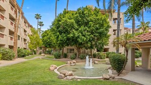 A courtyard with a fountain, palm trees, and a building with balconies. - Biltmore Condo w/ Heated Pool! (Phoenix)