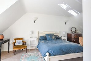 A bedroom with a white ceiling, a bed with blue bedding, a wooden chair, a small table, and a dresser. - Stable Cottage (Bridport)