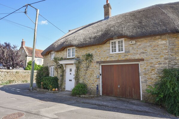 A stone house with a thatched roof, a wooden door, and a garage. - Stable Cottage (Bridport)