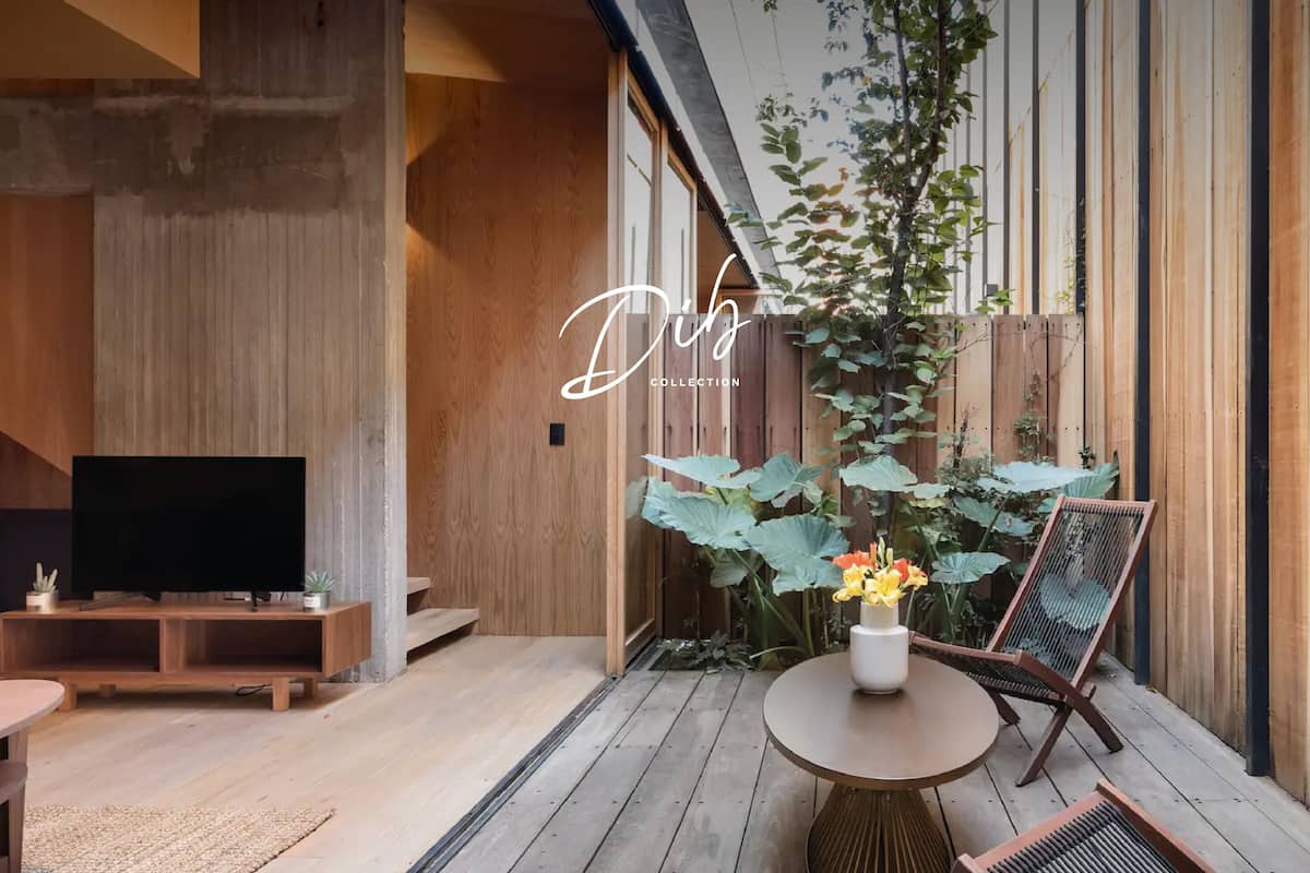 Una sala de estar moderna con un mueble de televisión de madera, un televisor de pantalla plana, una mesa redonda con un florero y una silla de mimbre.