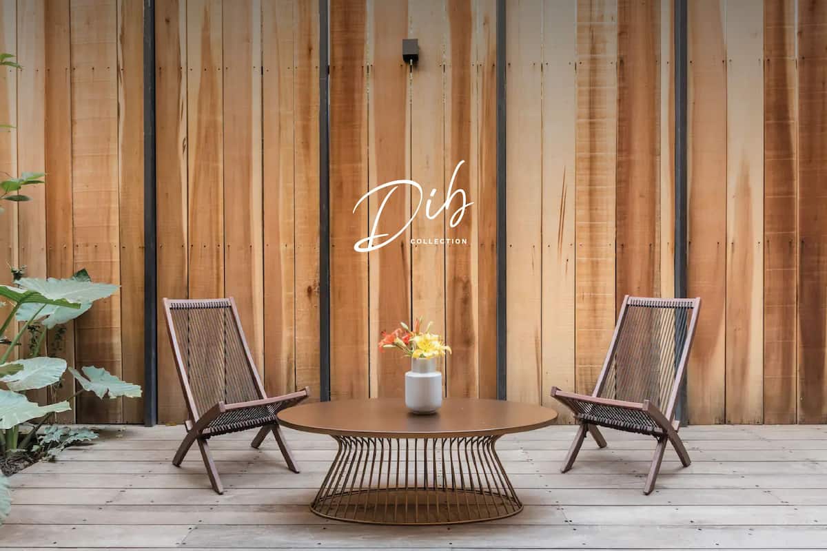 Una terraza de madera con dos sillas de mimbre y una mesa redonda con un florero.