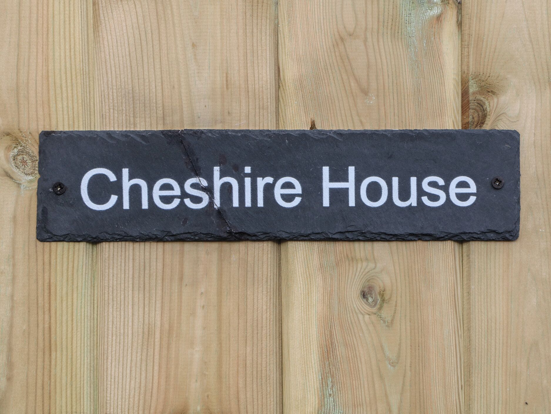 Une plaque noire en ardoise, avec des lettres blanches, portant l’inscription « Cheshire House », est fixée sur une surface en bois.