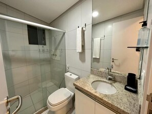 Un baño moderno con ducha de vidrio, inodoro blanco, lavabo con encimera de granito y espejo.