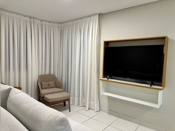 A living room with a flat-screen TV mounted on the wall, a beige armchair, and a white sofa. - HY Parque Atlântico (Recife)