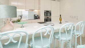 A modern kitchen with white cabinets, a central island with bar stools, a coffee machine, and an oven.
