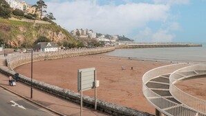 A coastal promenade with a sandy beach, a curved white railing, and a stone wall.