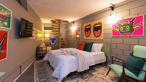 Ein Schlafzimmer mit einem Bett, einem Sessel, einer Wand mit farbenfroher Kunst und einer Wendeltreppe.