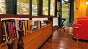 Ein Zimmer mit einer Holzhülle voller Bücher, einem roten Sessel und einem Fenster mit Jalousien.