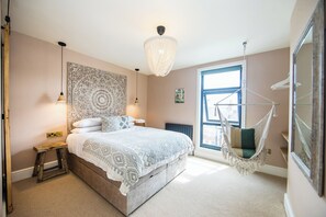 A bedroom with a bed, bedside lamps, a hanging chair, and a large window.
