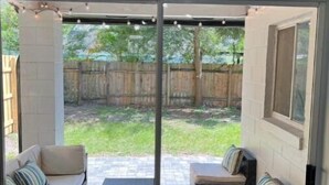 A patio area with a sofa set and a small table, a glass door leading to a backyard with a wooden fence and greenery. - Modern Universal Orlando (Orlando)