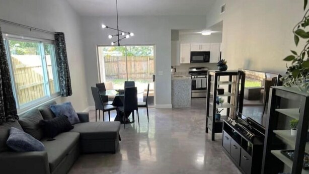 A modern living room with a grey sofa, a dining area with a glass table, and a kitchen with a TV and cabinets. - Modern Universal Orlando (Orlando)