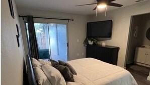 A bedroom with a bed, a ceiling fan, a TV mounted on the wall, and a sliding glass door leading to an outdoor area. - Modern Universal Orlando (Orlando)