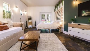 Une chambre moderne avec un lit, une table basse en bois, un canapé blanc, un téléviseur et une étagère à plantes fixée au mur.