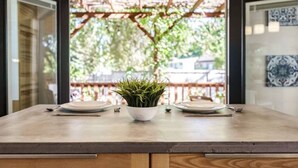 Une table à manger avec deux assiettes et une plante en pot au centre, le tout placé devant une terrasse en bois et une porte vitrée.