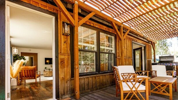 Une terrasse en bois avec des sièges d’extérieur, de grandes fenêtres et une pergola.