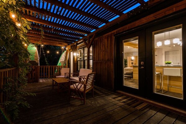 A wooden deck with outdoor seating and a view into a well-lit interior space.